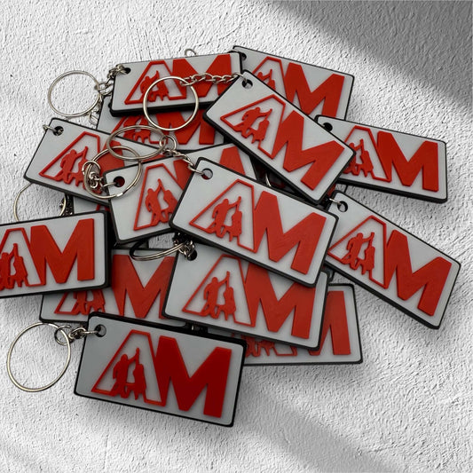 Multiple promotional AM keychains in red and white stacked together on textured surface